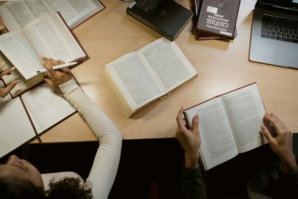 pexels photo 6549344 6549344 Group of adults studying together with open books and laptops on a wooden table.